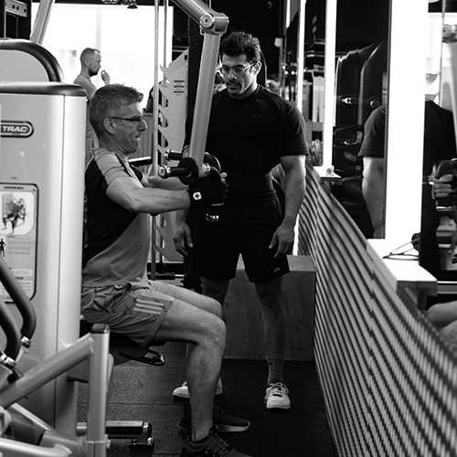 titans-gym-lelystad-balazs-personal-training-krachttraining-fitnessapparaat Balazs krijgt persoonlijke begeleiding van een personal trainer tijdens een krachttraining op een fitnessapparaat bij Titans Gym Lelystad.