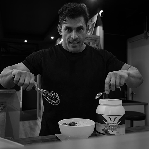 titans-gym-lelystad-hamed-parveh-lifestylecoaching-voedingsbegeleiding Hamed Parveh, lifestylecoach bij Titans Gym Lelystad, bereidt een gezonde maaltijd met eiwitpoeder en fruit tijdens voedingsbegeleiding.