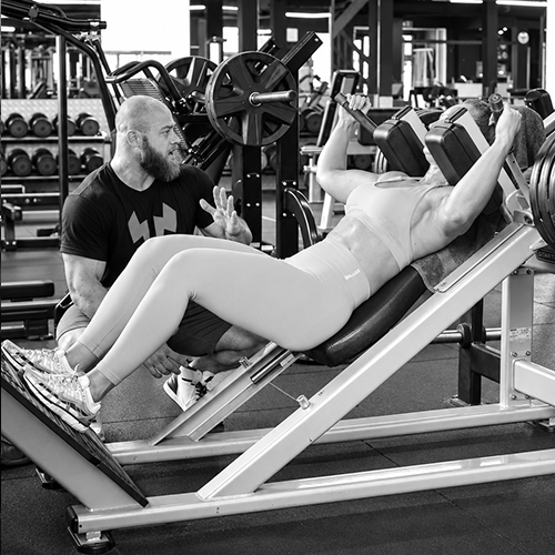 Personal trainer Rick begeleidt een sportster tijdens een leg press oefening bij Titans Gym Lelystad.